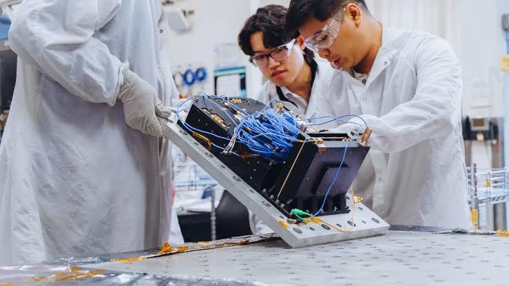 Two engineers place a wired electronic assembly onto a baseplate.